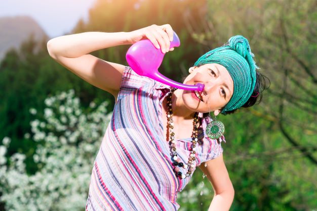 mladá žena so zelenou šatkou ukazuje s úsmevom aké ľahké je použiť nosovú sprchu
