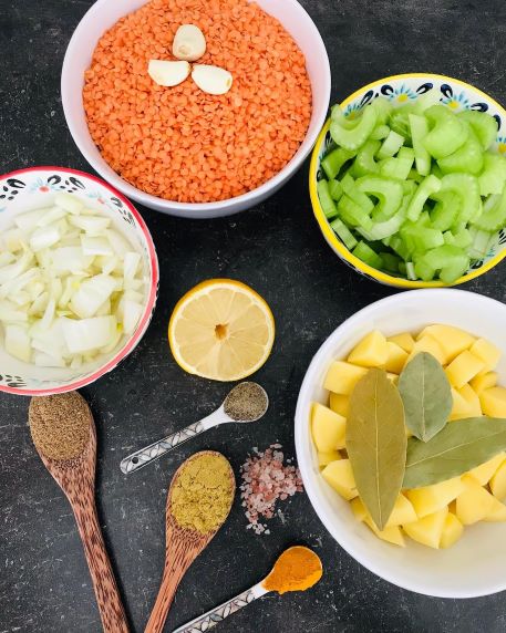 Ingrediencie na šošovicovú polievku v miskách sú červená šošovica, stopkový zeler, zemiaky, cibuľa, koreniny a citrón.
