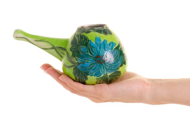 keramická konvička na preplach nosa zelenej farby s maľovaným kvetom položená na ruke
