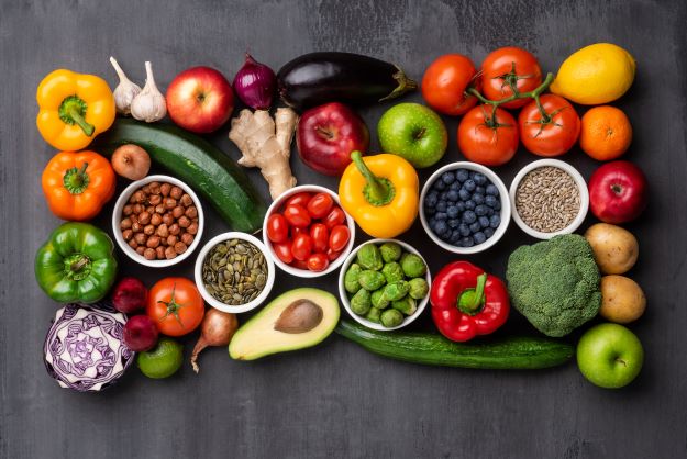 Na sivom stole sú voľne položené zdravé potraviny, farebné ovocie a zelenina