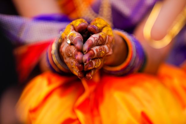 Ruky indickej ženy pomalované hennou súspojené dlaňami, ozdobené farebnými náramkami a sú posypané žltým kurkumovým práškom.