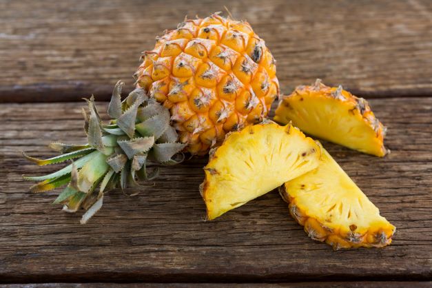 Na dreve je položený celý ananás, vedľa neho sú kúsky rozpoleného ananásu žltej farby.