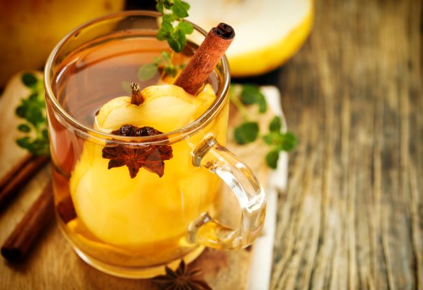 V sklenenom hrnčeku, ktorý je položený na drevenom stole je čaj s kúskom hrušky, drievkom škorice a s korením badiánu.
