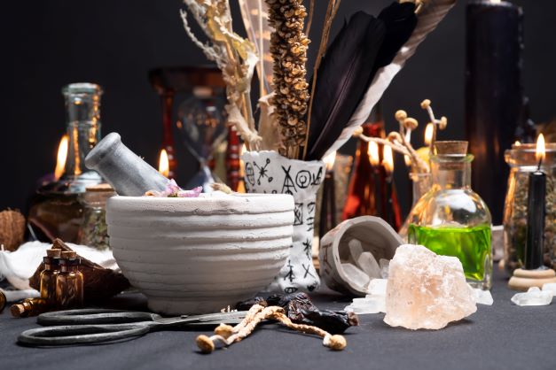 na stole je položená biela keramická miska, okolo sú rôzne liečivé bylinky a, sviečka a odvary.