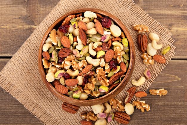 Vlašské orechy, mandle, kešu, pekanové orechy, pistácie sú naservírované v hnedej hlinenej miske, ktorá je položená na kúsku jutového vreca.