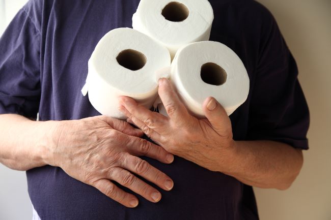 Tri rolky toaletného papiera drží muž v tmavomodrom tričku s ľavou rukou na bruchu, pravou si drží žalúdok.