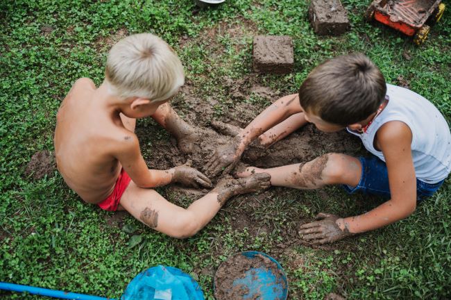 Dvaja chlapci sa v lete hrajú v na zemi, sú zablatení od hliny.