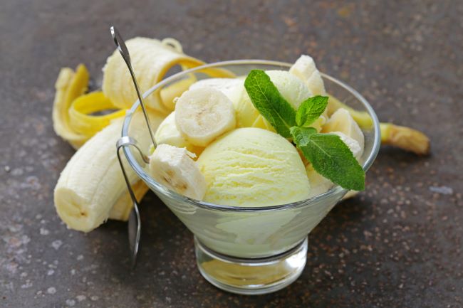 V sklenenom pohári sú kopečky banánovej zmrzliny s kúskami čerstvého banánu, ozdobené mätou.