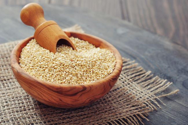 Biela quinoa v drevenej miske, ktorá je položená na kúsku vreca.
