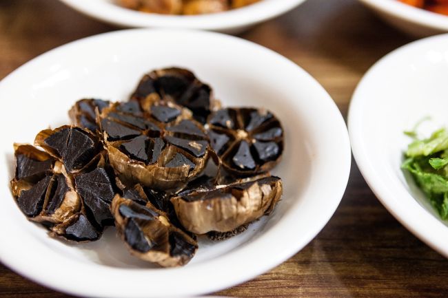 Fermentovaný čierny cesnak na bielom tanieri ako súčasť zdravej výživy. Fermentovaný čierny cesnak má blahodárne účinky na zdravie