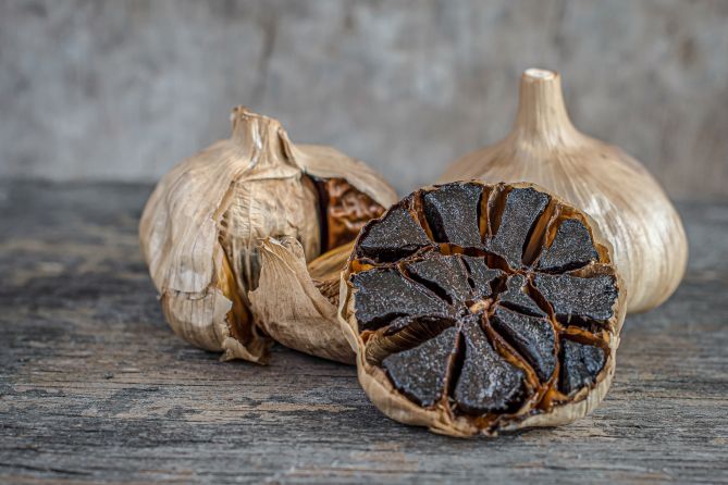 Čierny cesnak na drevenom rustikálnom stole. Fermentovaný čierny cesnak a jeho účinky.